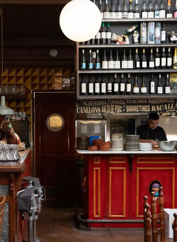 Barra i cuina oberta de La Taverna del Mercantic, amb prestatgeria de vins